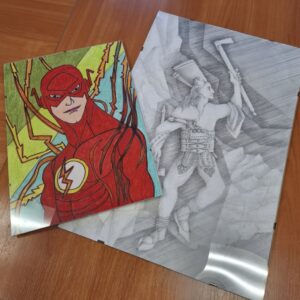 Rysunki przedstawiające postać superbohatera w czerwonym kostiumie oraz stylizowaną grafikę przedstawiającą mitologicznego wojownika, leżące na drewnianym stole.