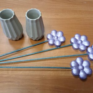 Dwóch ceramicznych wazonów oraz pięć metalowych kwiatów w kolorze lawendy na tle drewnianego blatu.